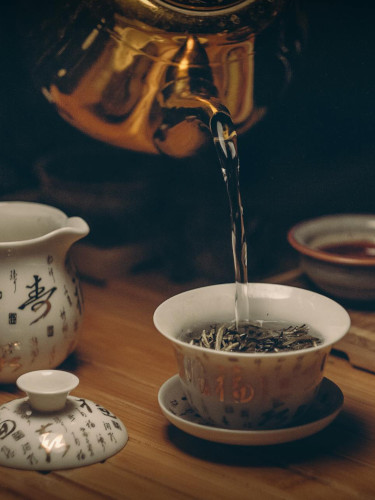 Two smiling women; one is pouring tea for her friend who's holding a book she's been reading.