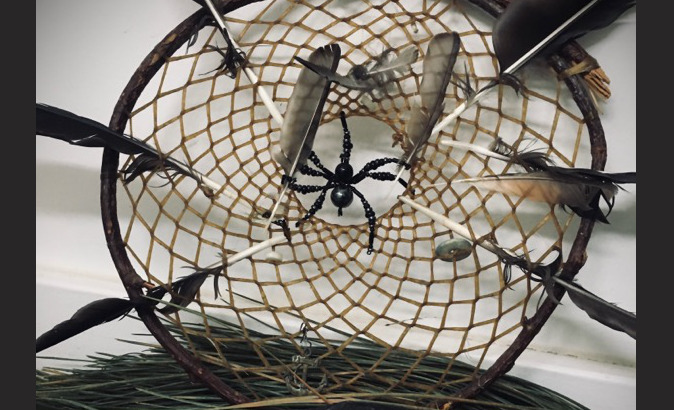 A dreamcatcher with a spider at the center, surrounded by six feathers. A large piece of obsidian sits below.